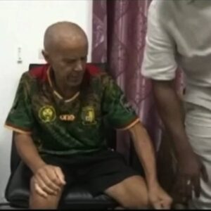 Francés detenido en Guinea Ecuatorial, sentado en un despacho con la camiseta de Camerún junto a un hombre de pie, en una emisión de TVGE