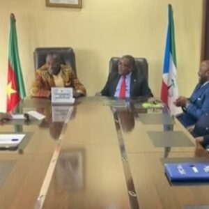 Reunión en una sala de juntas con las banderas de Camerún y Guinea Ecuatorial, durante la visita del embajador Kote al gobernador de la región del Sur de Camerún